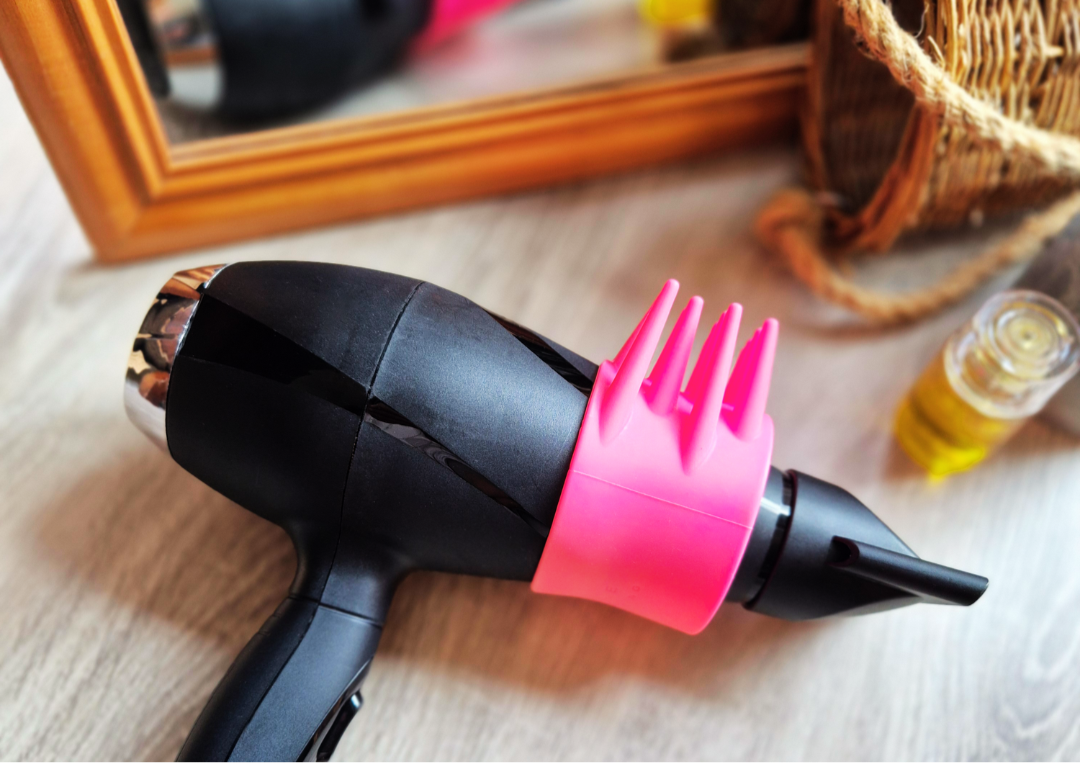 Black hair dryer with pink dryspike attachment on a wooden surface.
