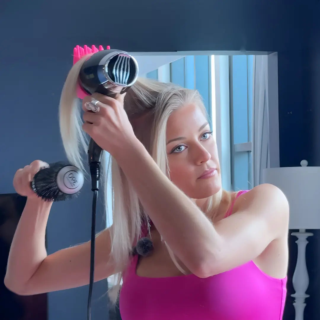 Woman in pink top using a hair dryer with dryspike blowout tool attachments in a room.