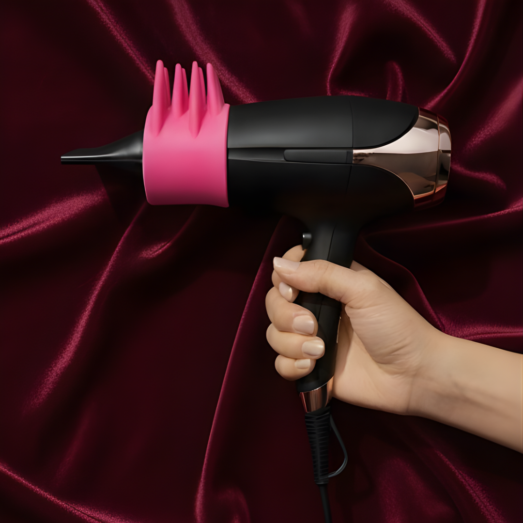 Hand holding a hair dryer with a pink dryspike tool against a red fabric background